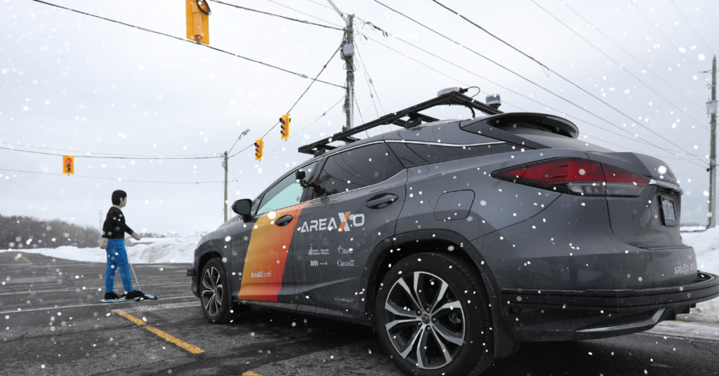 An autonomous vehicle is stopped at an intersection as a simulated pedestrian crosses at a crosswalk in snowy weather.