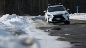 An autonomous vehicle splashes through a puddle in snowy conditions. 