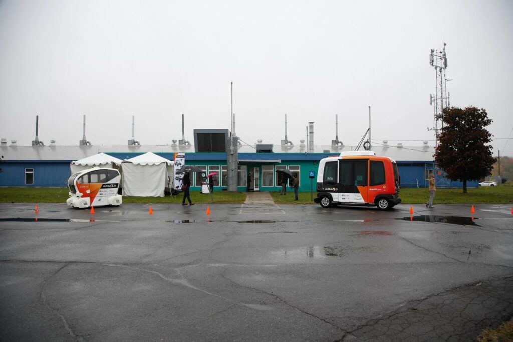 Autonomous vehicles are parked out front of a building on a rainy, overcast day.