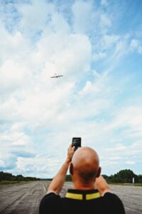 A photo taken from over the shoulder of a man, filming the flight of drones with his phone. 